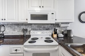 A kitchen with white cabinets, a microwave, a stove, and a granite countertop. - 🏖️ Grand Caribbean 423 | 2BR Orange Beach | Steps to Beach + Pool + Fitness (Orange Beach)