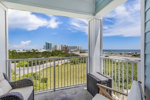 A balcony with a view of a beach, a road, and buildings in the distance. - 🏖️ Grand Caribbean 423 | 2BR Orange Beach | Steps to Beach + Pool + Fitness (Orange Beach)