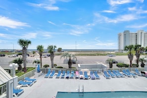 A rooftop pool area with blue lounge chairs, a pool, and a view of the beach and road. - 🏖️ Grand Caribbean 423 | 2BR Orange Beach | Steps to Beach + Pool + Fitness (Orange Beach)