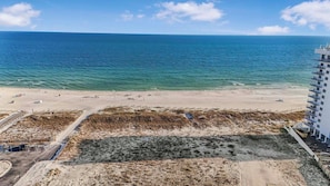 Ein Strand mit sandigem Ufer und einem Gebäude mit mehreren Balkonen, die auf den Ozean blicken.