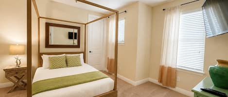A four-poster bed with a ceiling fan, a television, and a green vase on a dresser.