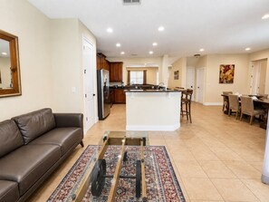 A spacious living room with a leather sofa, a glass coffee table, and a patterned rug. - Private Pool & Spa | Game Room | Sleeps 13 (Kissimmee)