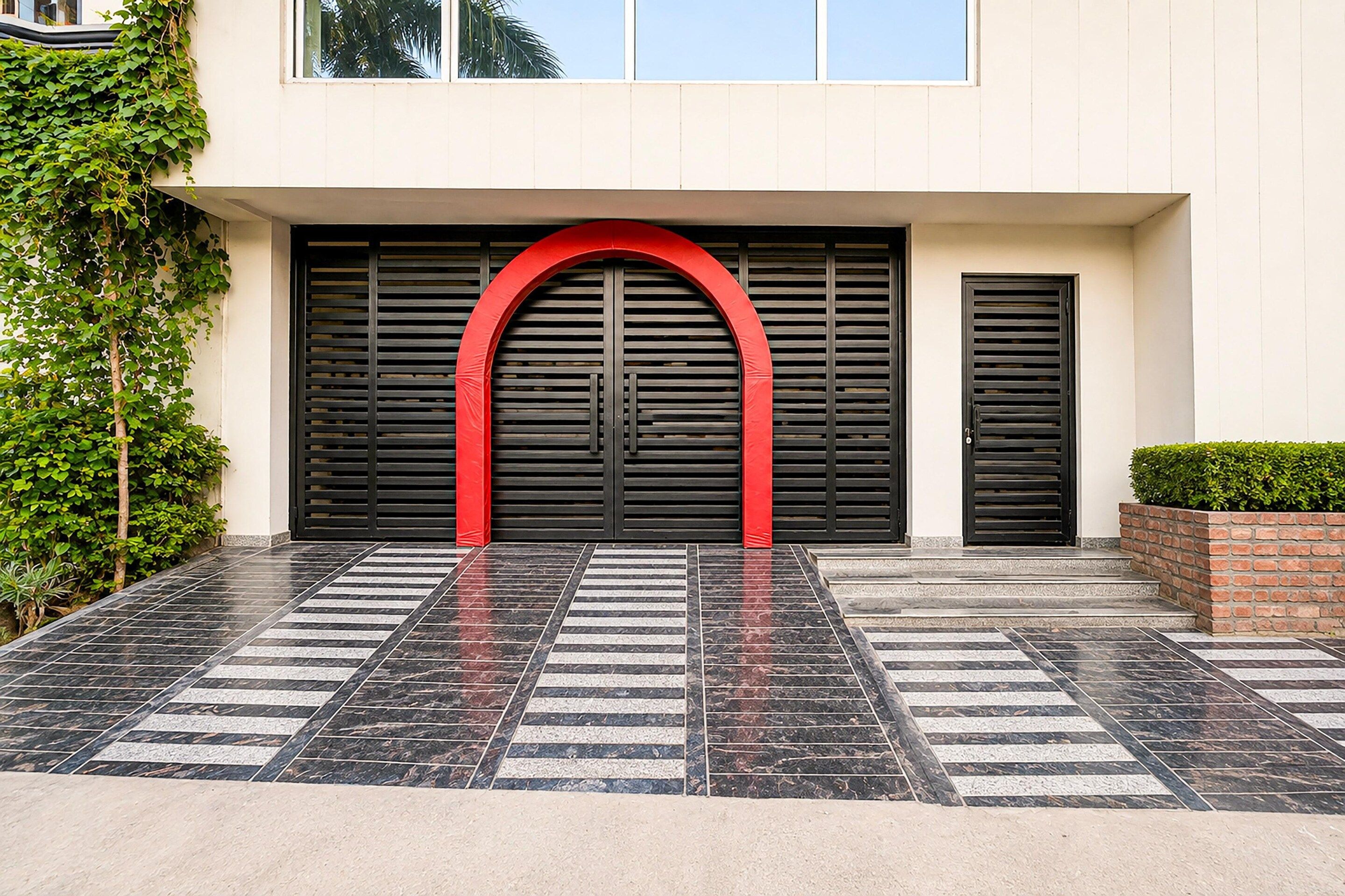A modern building entrance with a red archway, black shutters, and a tiled pavement.