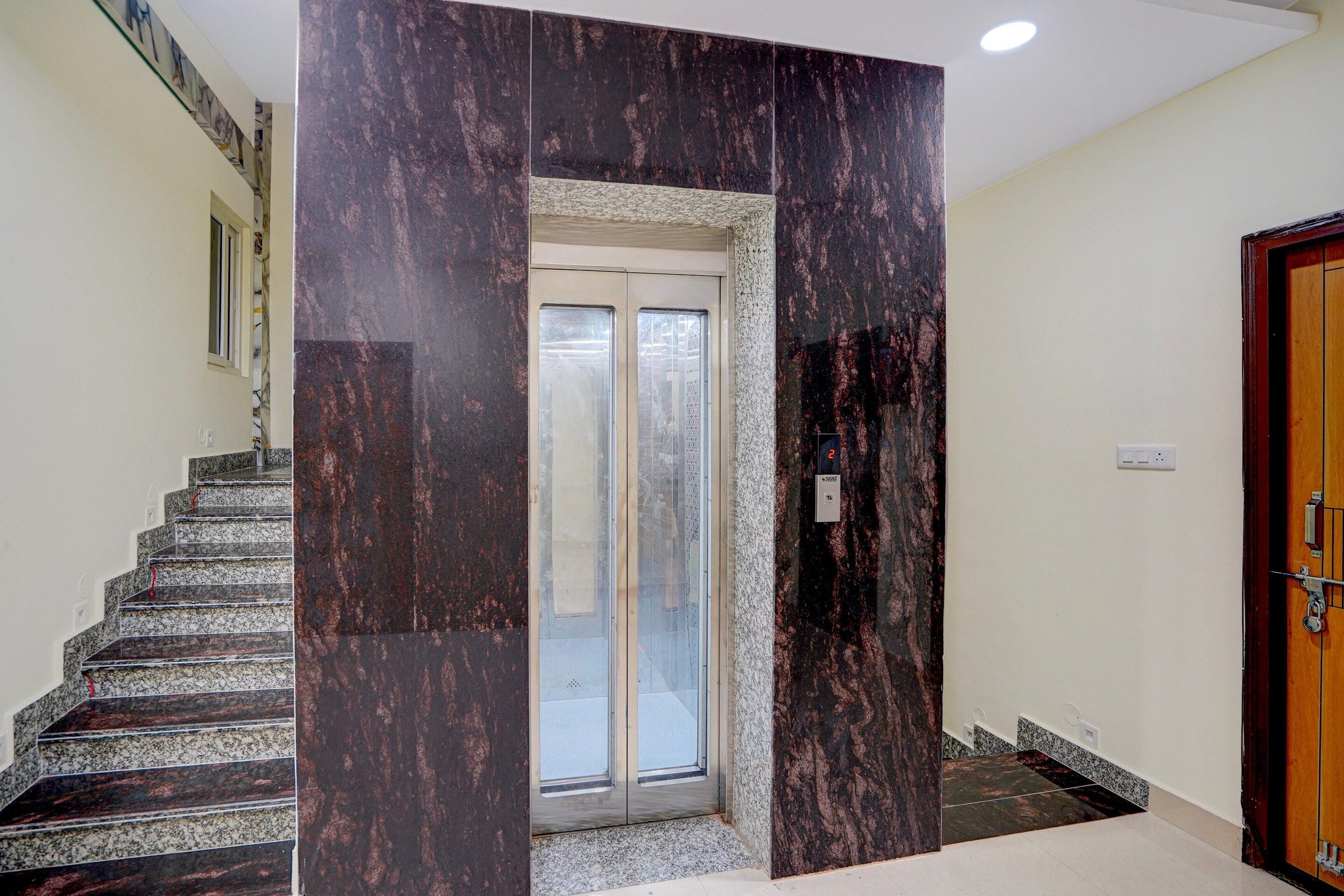 A staircase with a marble wall, a door with a glass panel, and a wooden door on the right.