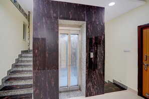 Una escalera con un muro de mármol, una puerta con un panel de vidrio y una puerta de madera a la derecha.