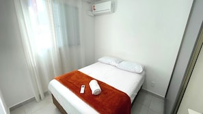 A hotel room with a bed, white curtains, a window, and an air conditioning unit.