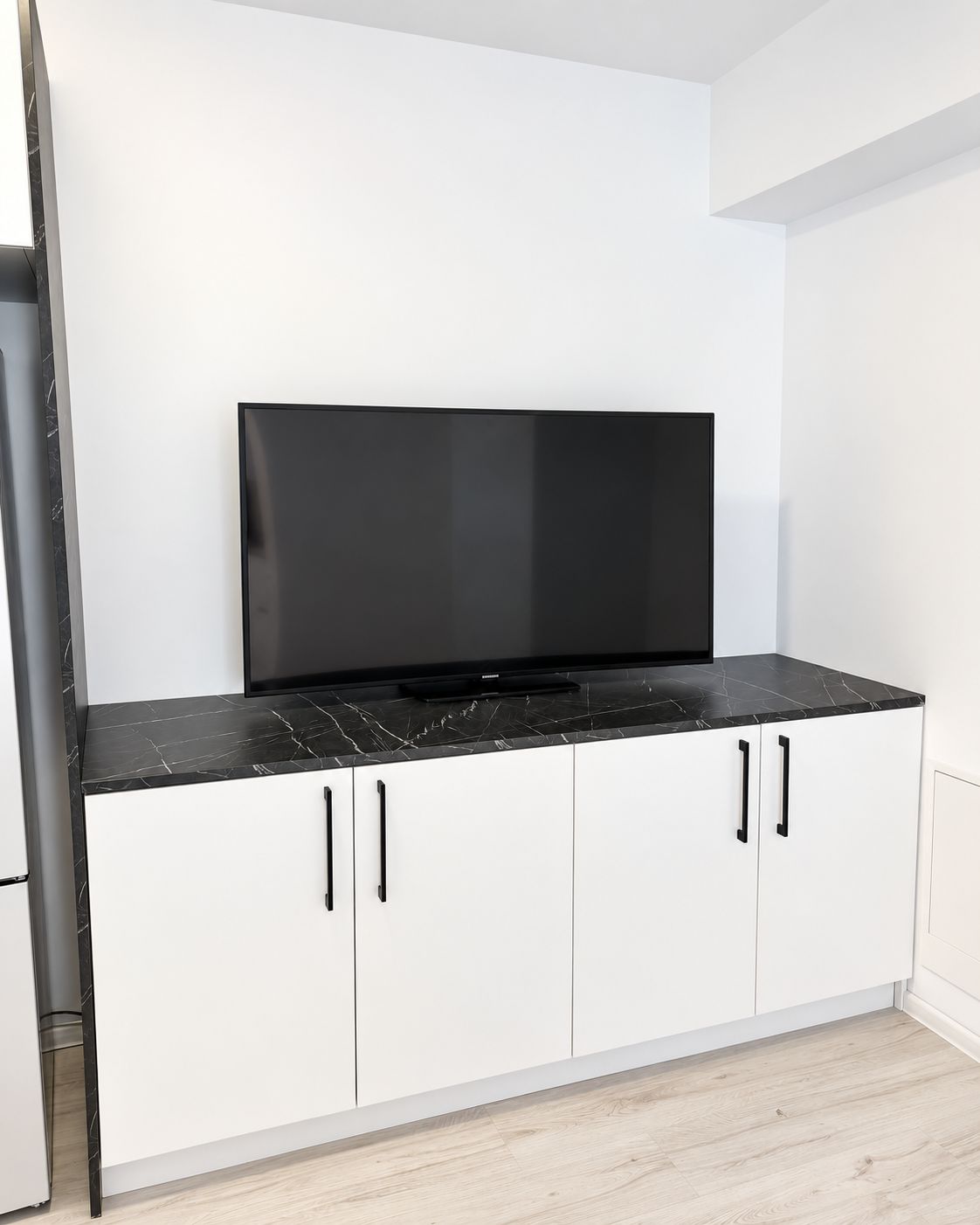 A kitchen with a black countertop, white cabinets, and a flat-screen TV mounted above the cabinets.