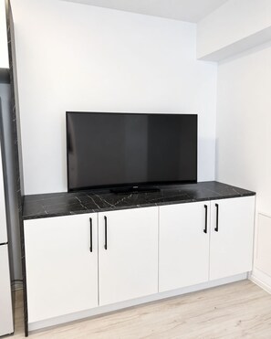 Cuina amb taulell negre, armaris blancs i televisió de pantalla plana penjada sobre els armaris.