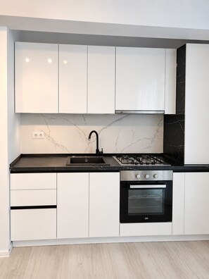 Une cuisine moderne avec des meubles blancs, un plan de travail noir, une cuisinière à gaz et un four.