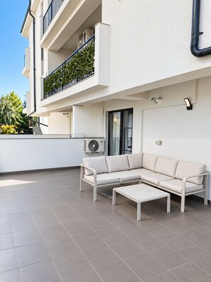A modern outdoor living area with a white sofa and a matching table, a balcony with a black railing, and an air conditioning unit. - Myonna Style AIRPORT 1 - Otopeni - Therme (Otopeni)