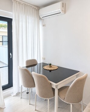 Un espace repas moderne avec une table noire, quatre chaises de couleur beige et un appareil de climatisation fixé au mur.