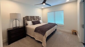 A bedroom with a bed, bedside table, lamp, ceiling fan, window with blinds, and a small stool. - 4-bedroom condo on Lone Peak mountain.  Not near the mountain. On it! (Big Sky)