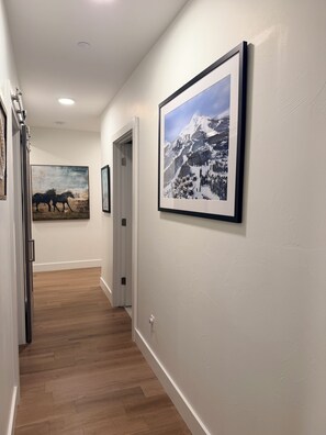 A hallway with wooden flooring, white walls, and framed pictures including a mountain landscape and a horse painting. - 4-bedroom condo on Lone Peak mountain.  Not near the mountain. On it! (Big Sky)