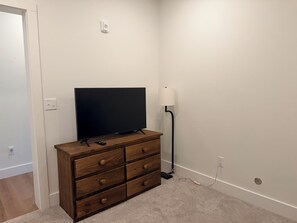 Ein Zimmer mit einem hölzernen Schminktisch, einem Fernseher, einer Lampe und einem Teppichboden.