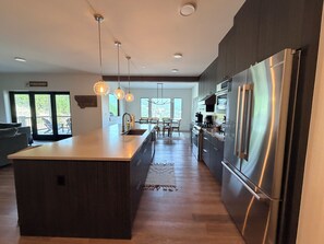A modern kitchen with a central island, stainless steel appliances, pendant lighting, and a view to the outdoors. - 4-bedroom condo on Lone Peak mountain.  Not near the mountain. On it! (Big Sky)
