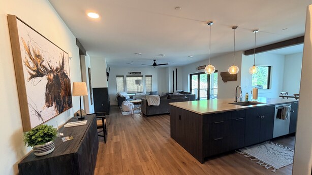 A modern kitchen with a central island, wooden flooring, pendant lighting, and a view to a deck area. - 4-bedroom condo on Lone Peak mountain.  Not near the mountain. On it! (Big Sky)