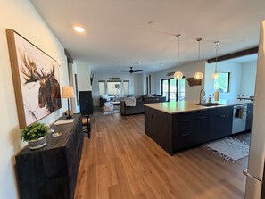 A modern kitchen with a central island, wooden flooring, pendant lighting, and a view to a deck area. - 4-bedroom condo on Lone Peak mountain.  Not near the mountain. On it! (Big Sky)