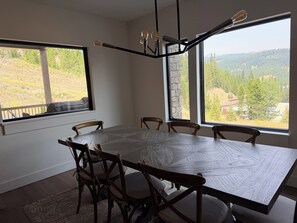 A dining area with a large table and chairs, large windows with a view of a hilly landscape. - 4-bedroom condo on Lone Peak mountain.  Not near the mountain. On it! (Big Sky)