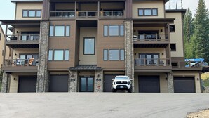 A multi-story building with a stone facade, multiple balconies, and a parking area with a white vehicle. - 4-bedroom condo on Lone Peak mountain.  Not near the mountain. On it! (Big Sky)