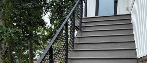 A set of grey wooden stairs with a black metal handrail and a stone wall on one side.