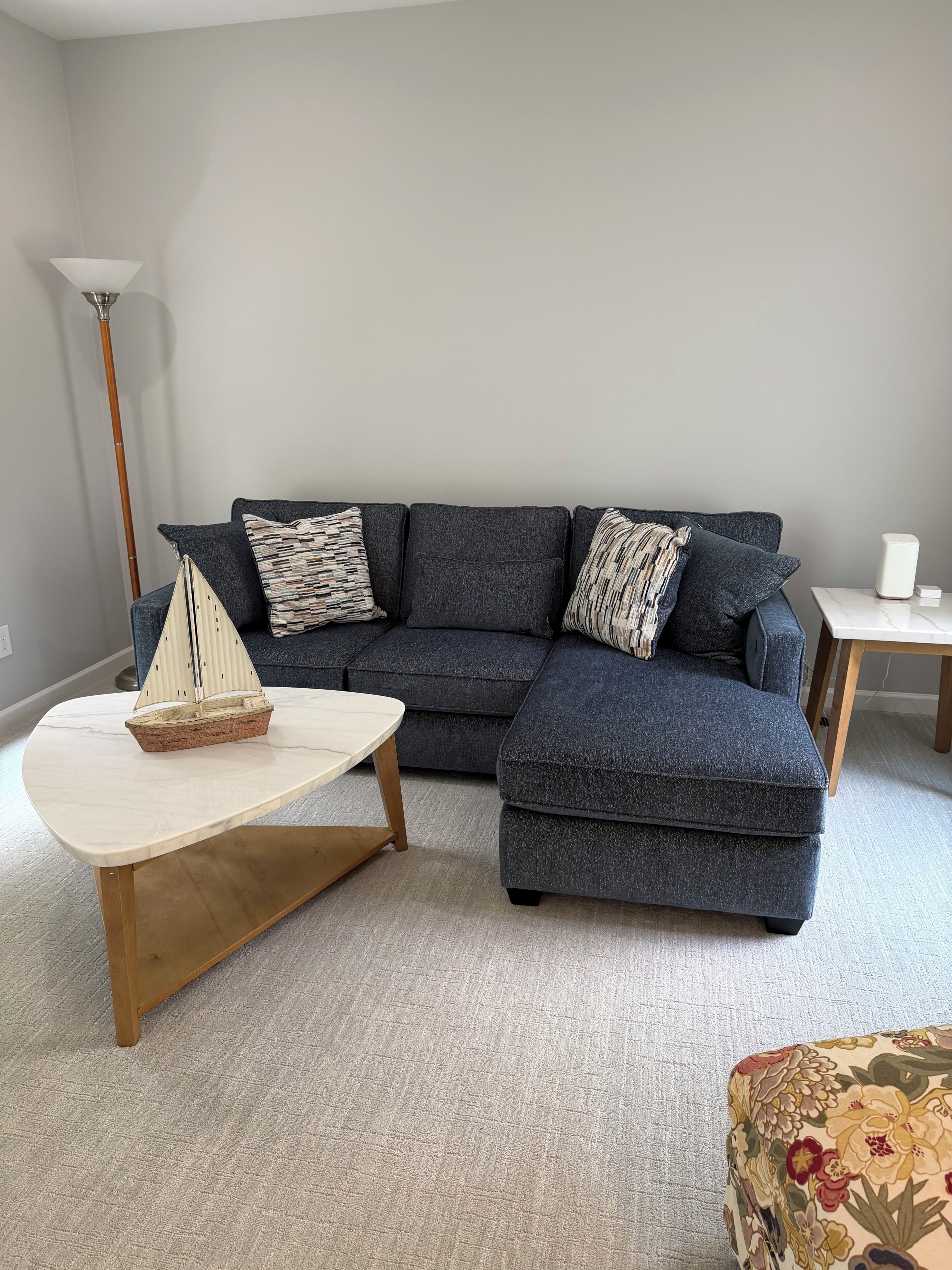 A living room with a sectional sofa, a small coffee table, a decorative sailboat, and a lamp.