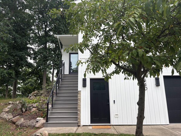 A modern two-story house with a staircase leading to the entrance, surrounded by trees and a stone wall. - Private Lakeview Retreat on 1+ Acre - Quiet, Scenic, Close to Everything (Augusta)