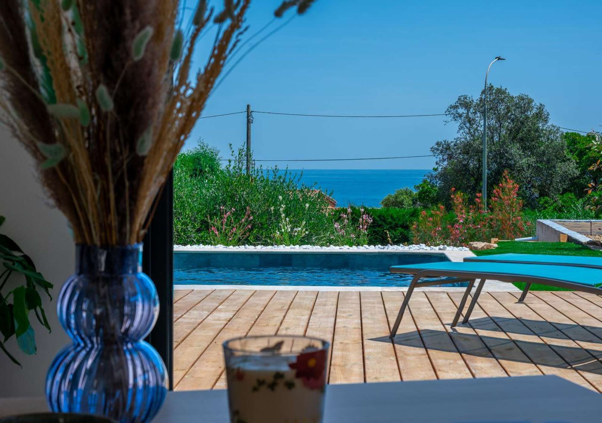 Blick auf einen Pool mit freiem Blick aufs Meer, eine Holzterrasse und ein Getränk.