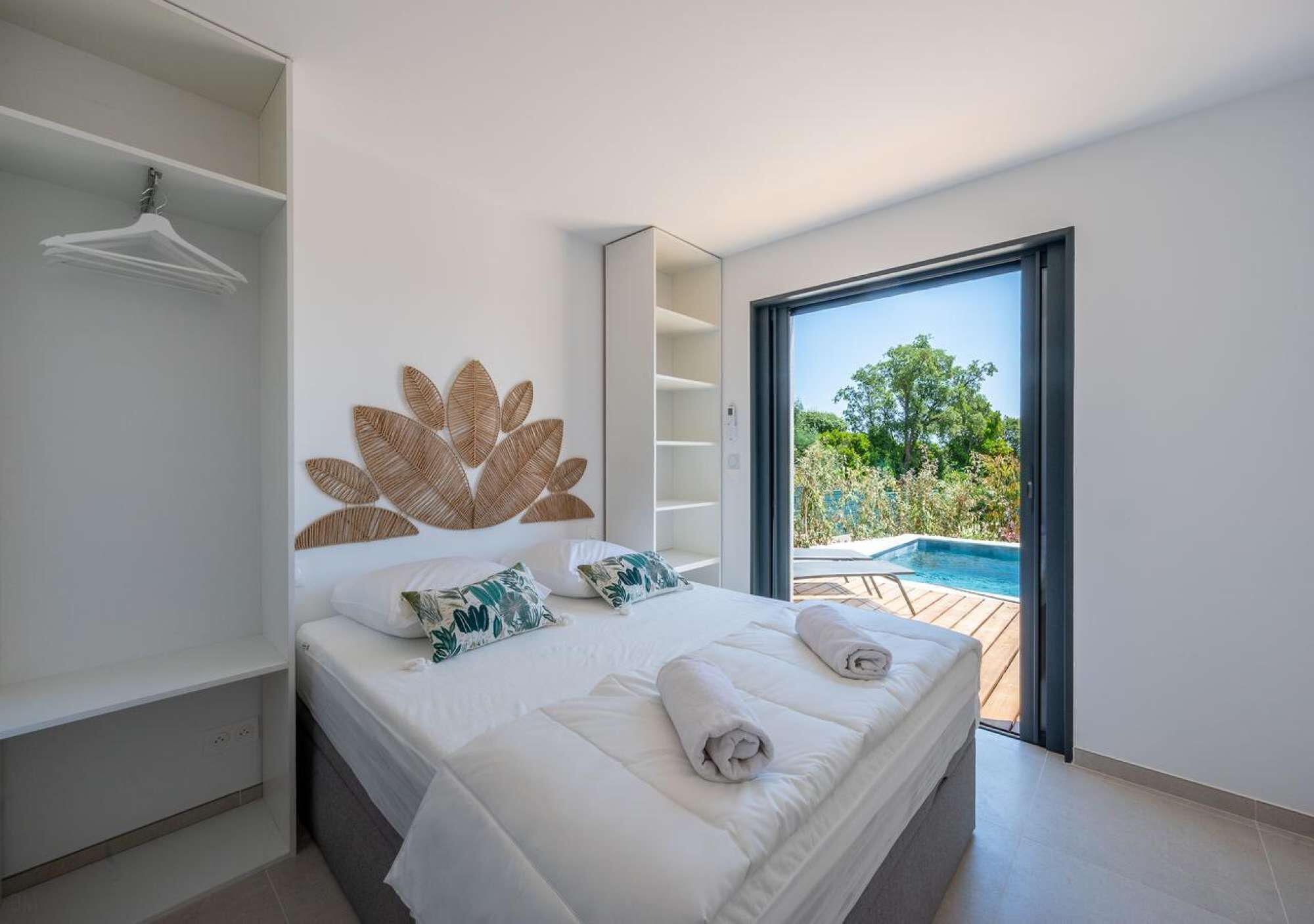 Een moderne slaapkamer met een groot bed, een wandplank en uitzicht op een buitenzwembad.