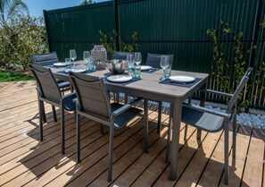 Een houten terras met een eettafel, omringd door stoelen.