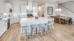 Una cucina moderna con mobili bianchi, un'isola centrale con sgabelli da bar e un'area pranzo con tavolo e sedie in legno.