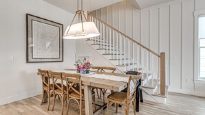Zona pranzo con tavolo e sedie in legno, un lampadario, un'opera d'arte incorniciata e una scala con ringhiere bianche.