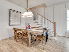 Ein Essbereich mit einem Holztisch und Stühlen, einer Kandelaber, einem gerahmten Kunstwerk und einer Treppe mit weißen Geländern.