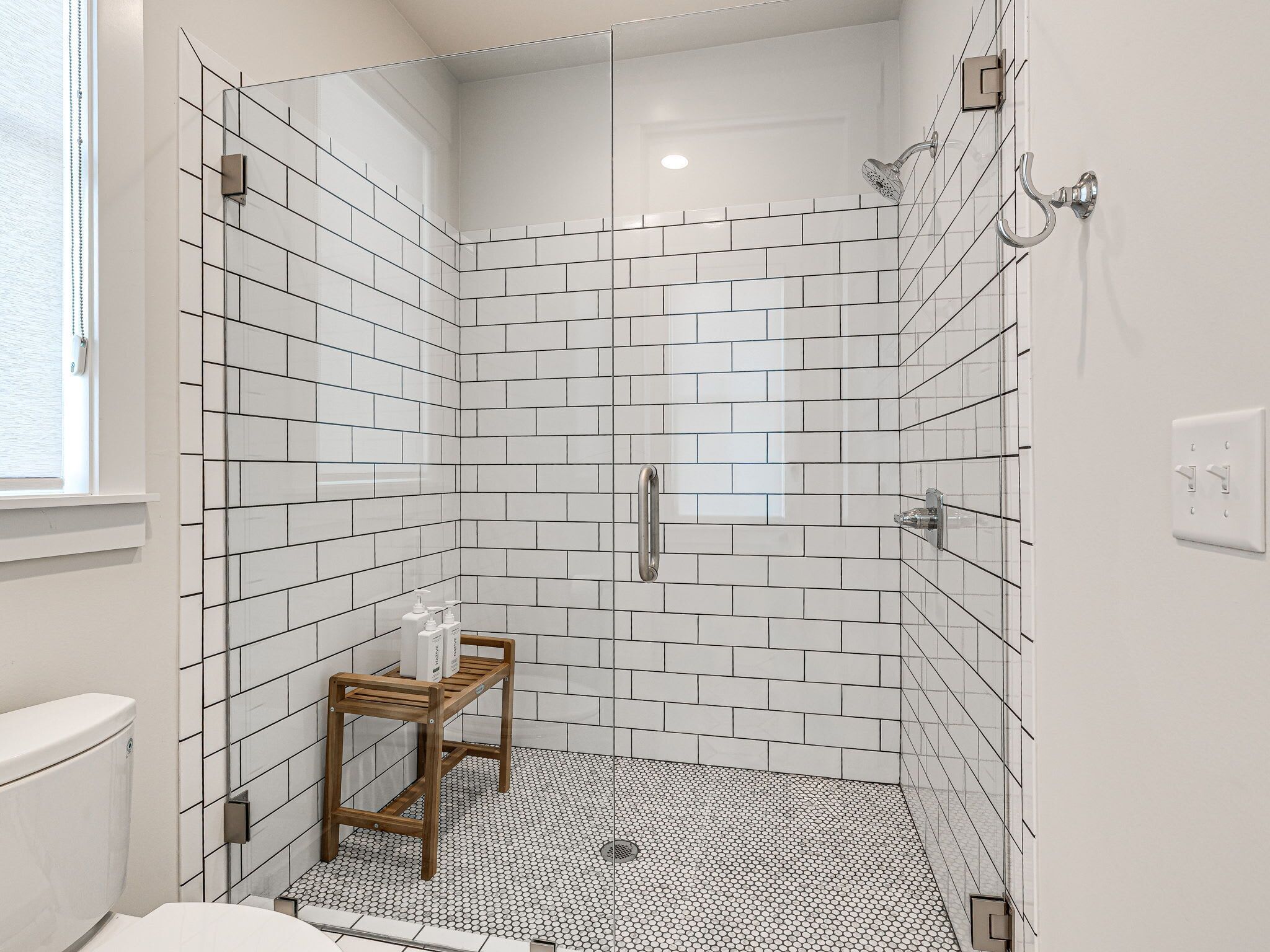 A modern bathroom with white subway tiles, a wooden bench, and a handheld showerhead.