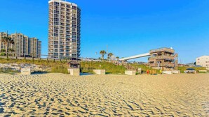 A sandy beach with a tall hotel structure and a partially constructed building. - Beach View Studio with Private Balcony, Pool, Hot Tub & Resort Access (Miramar Beach)