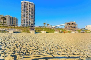 Ein sandiger Strand mit einem hohen Hotelgebäude und einem teilweise errichteten Bau.