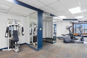 Ein Fitnessraum mit Trainingsgeräten, einer Spiegelwand und Blick ins Freie.