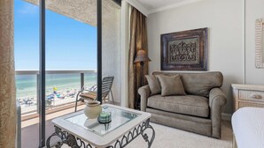 A balcony with a view of the beach, a sofa, a lamp, and a framed artwork. - Beach View Studio with Private Balcony, Pool, Hot Tub & Resort Access (Miramar Beach)