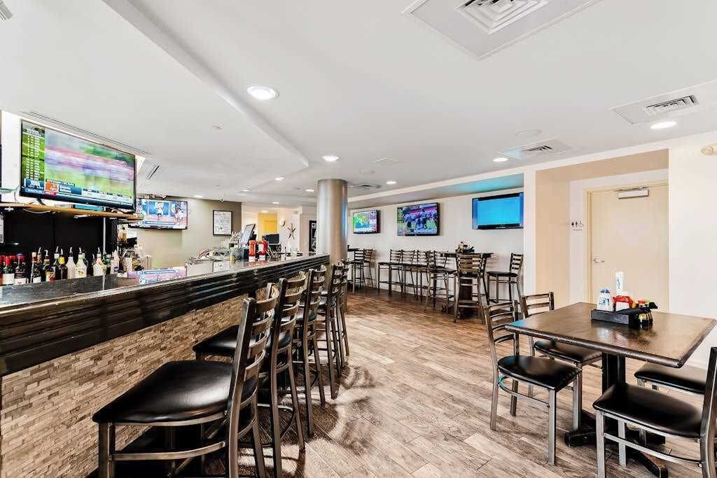 Eine Bar mit mehreren Fernsehern, einer Theke voller Flaschen und einigen Tischen mit Stühlen.