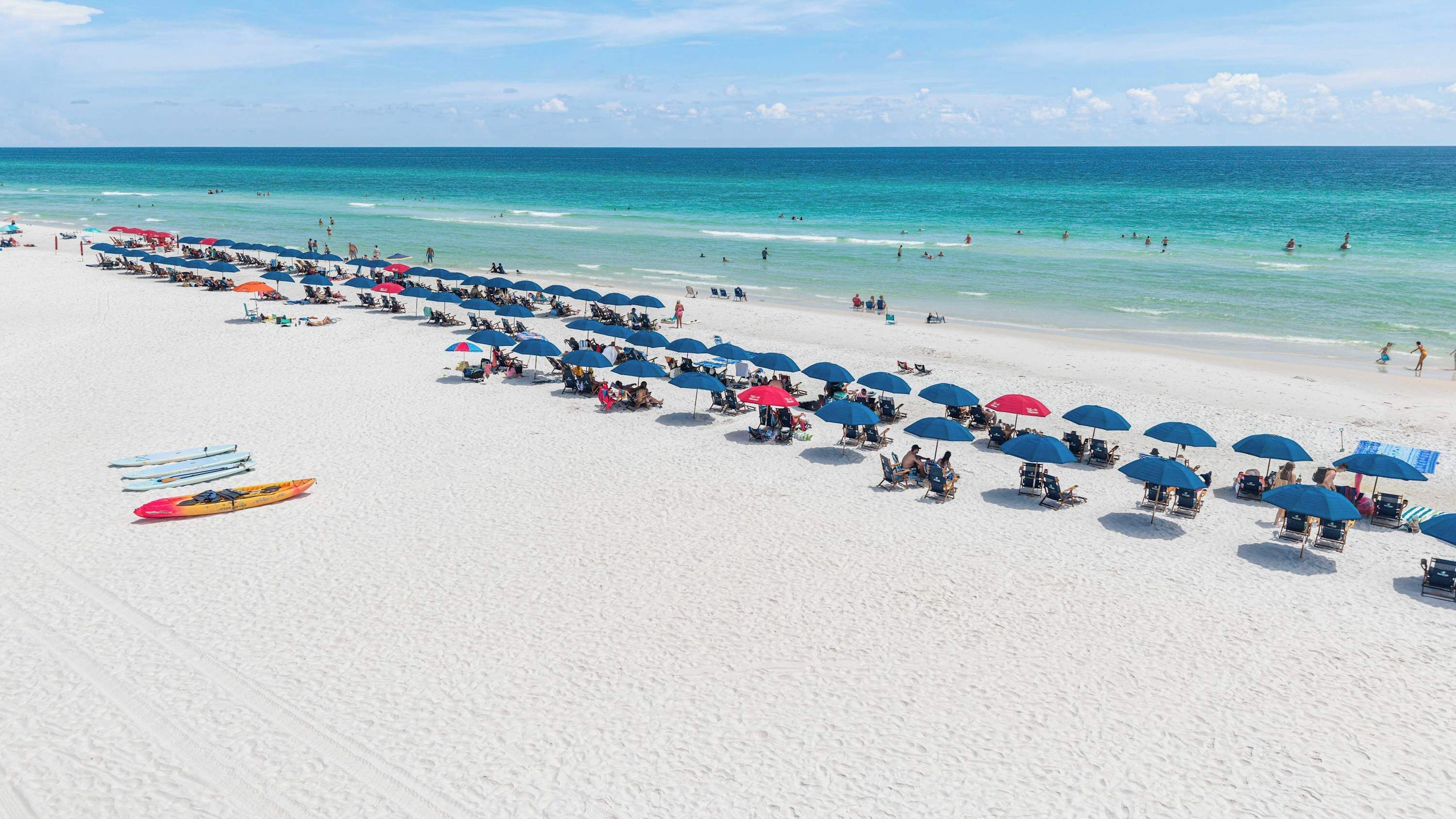 Ein Strand mit Reihen von Sonnenschirmen und Liegestühlen, einem klaren Himmel und dem Ozean im Hintergrund.