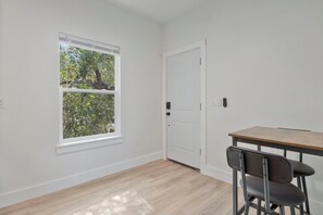Habitació amb una finestra gran, una porta, taula i cadires, i un sòl de tons clars.