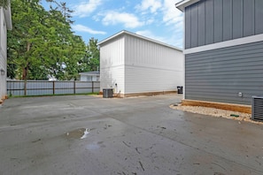A concrete patio area with a fence, a building with white siding, and a tree in the background. - The Graffiti Loft - Artsy 1BR Near Downtown Pensacola (Pensacola)