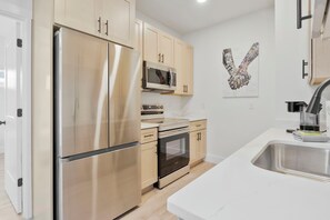 A modern kitchen with stainless steel appliances, wooden cabinets, and a white countertop. - The Graffiti Loft - Artsy 1BR Near Downtown Pensacola (Pensacola)