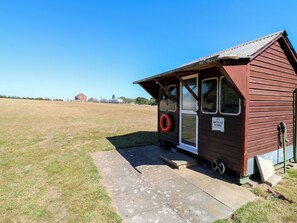 A small wooden building with a sign indicating a bicycle store, a lifebuoy hanging on the door, and a clear sky in the background. - Lakewood Plot 9 (Clacton-on-Sea)