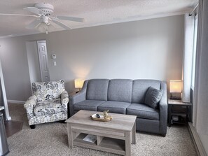 A living room with a grey sofa, patterned armchair, and a coffee table with a remote control. - Ski IN/Ski OUT Snowshoe Rental (Snowshoe)