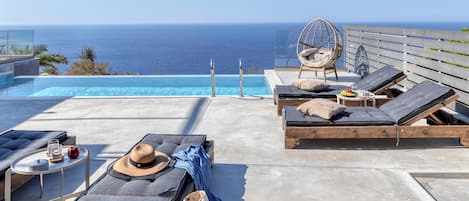 Une terrasse sur le toit avec une piscine, des chaises longues, un fauteuil suspendu et une table où sont servis des boissons et des collations.