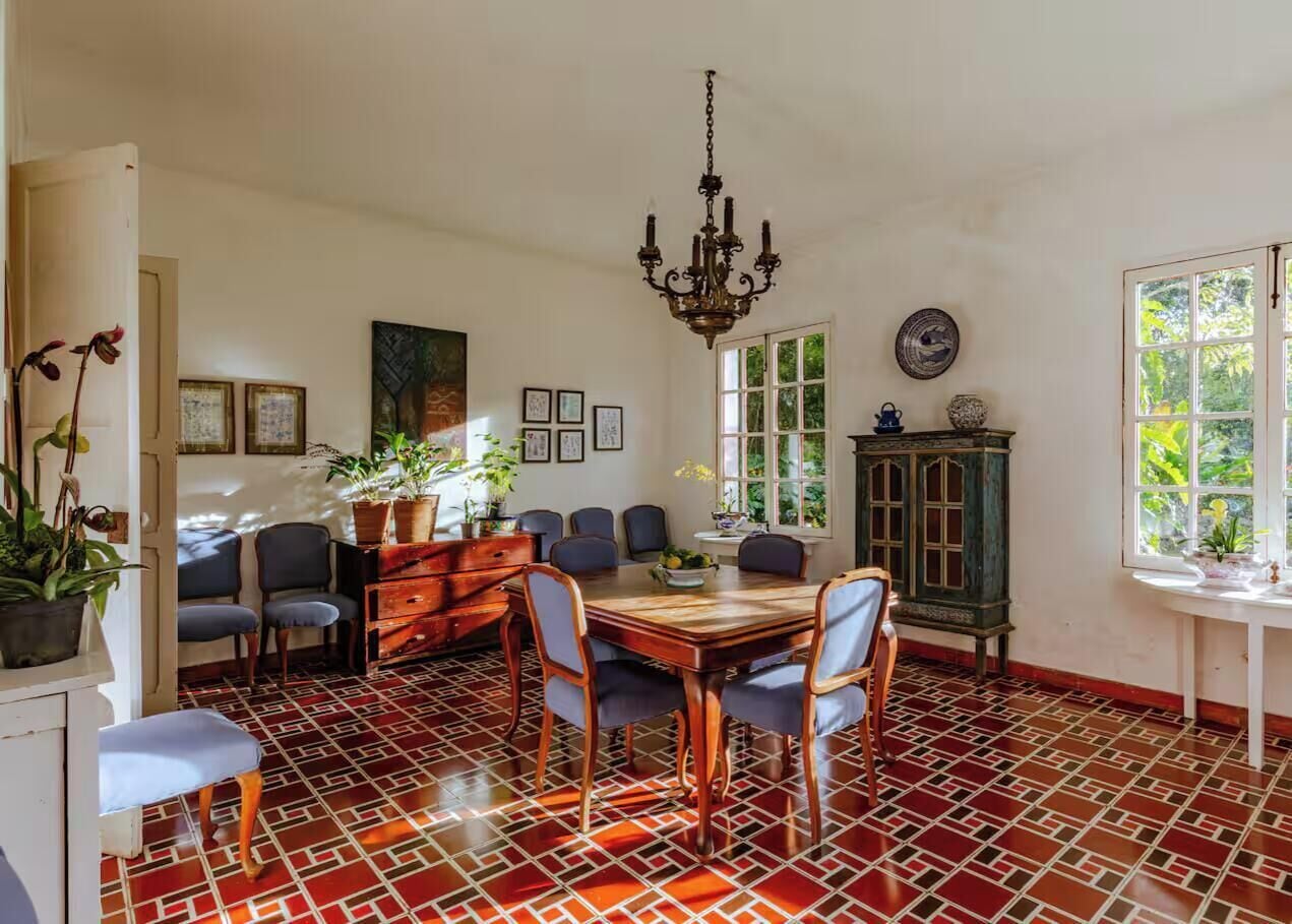 Un comedor con una mesa y sillas de madera, una lámpara de araña y un suelo estampado.