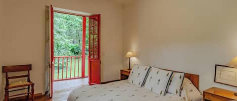 A bedroom with a bed, a chair, a nightstand, and a door leading to a balcony.