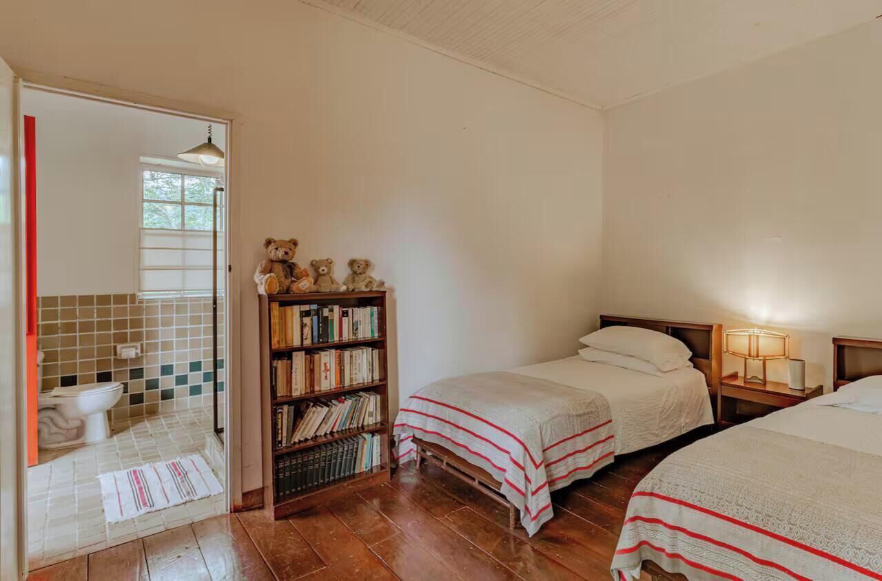 A room with two beds, a bookshelf, a mirror, and a bathroom with a toilet and sink.