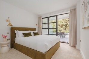 A bedroom with a large bed, a bedside table, a lamp, and a view of an outdoor area. - Sea Breeze by Grandeur Property (Poole)