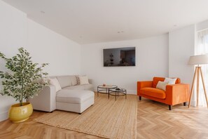 A living room with a sofa, an orange armchair, a coffee table, a floor lamp, and a potted plant. - Sea Breeze by Grandeur Property (Poole)